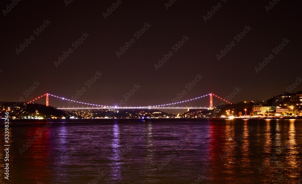 Istanbul Bosporus Bridge with colourful lights and its reflections on sea during night