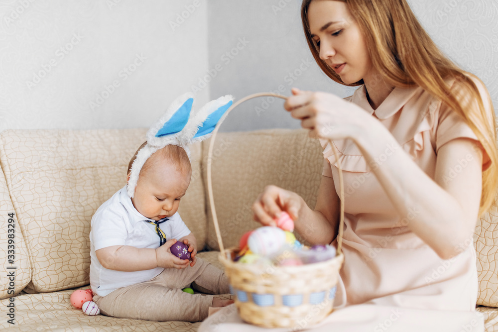 Mother and baby with rabbit ears, with Easter eggs in a basket, parents and children play indoors. Family celebrates Easter, Mother and baby with rabbit ears, with Easter eggs in a basket, parents and children play indoors. Family celebrates Easter,