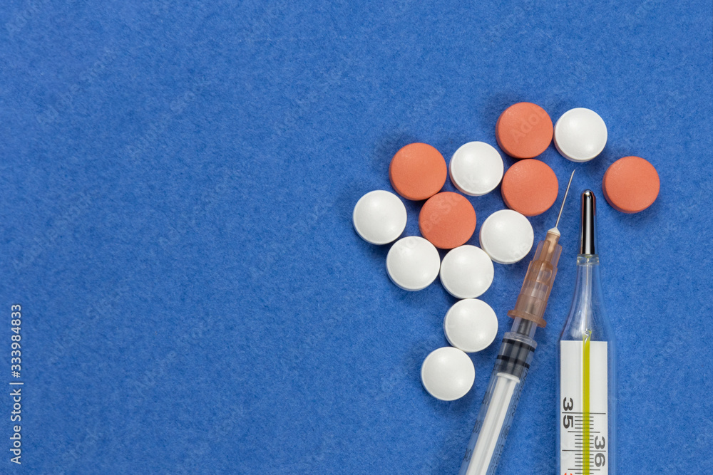 Syringe with injectable coronavirus vaccine solution on a blue background. Pills and vitamins. Medical thermometеr. COVID pandemic protection. Top view. Copy space Syringe with injectable coronavirus vaccine solution on a blue background. Pills and vitamins. Medical thermometеr. COVID pandemic protection. Top view. Copy space