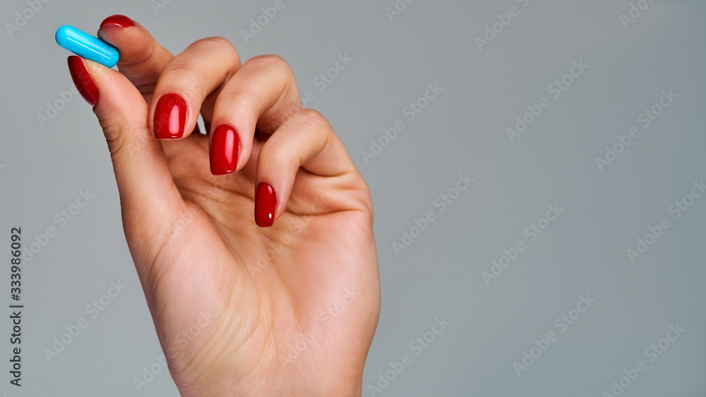 Female hand with red nails holds a blue pill in fingers. Medical concept Female hand with red nails holds a blue pill in fingers. Medical concept