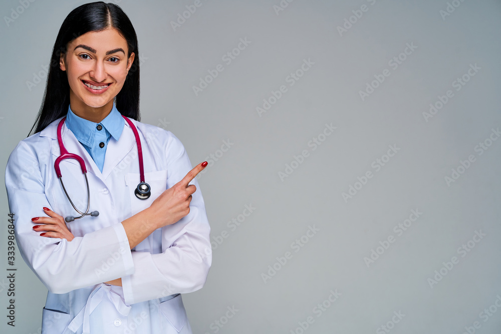 Happy girl with a phonendoscope on her neck looking at camera and points finger right. Medical concept Happy girl with a phonendoscope on her neck looking at camera and points finger right. Medical concept