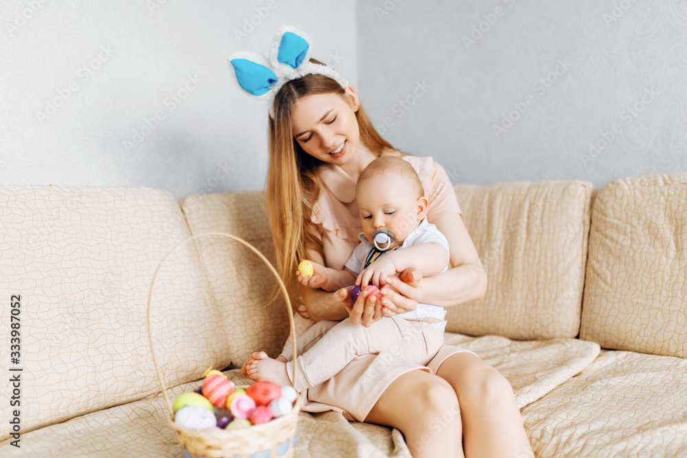Mother and baby with rabbit ears, with Easter eggs in a basket, parents and children play indoors. Family celebrates Easter, Mother and baby with rabbit ears, with Easter eggs in a basket, parents and children play indoors. Family celebrates Easter,