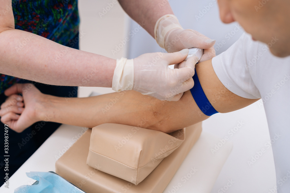 Obraz premium Nurse tightening the medical tourniquet on arm before taking blood sample. Preparation for blood test with by phlebotomist technician doctor. Concept of healthcare and medicine.