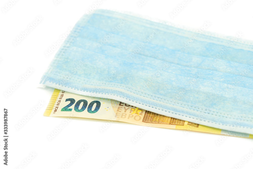 Obraz premium A blue medical mask lies on a banknote of 200 euros. Concept of buying a mask in Europe, protection against the virus. Isolated white background.