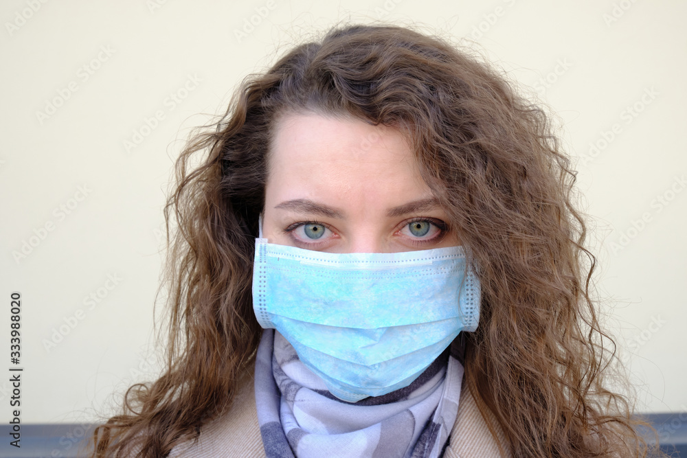 The girl's face with curly hair in a medical mask closeup. the emotions of the patient The girl's face with curly hair in a medical mask closeup. the emotions of the patient