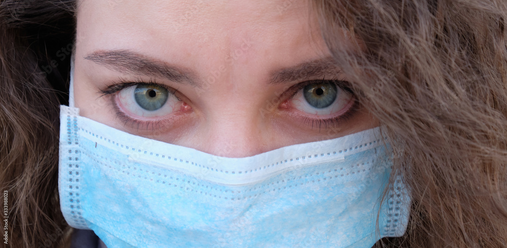 The girl's face with curly hair in a medical mask closeup. the emotions of the patient The girl's face with curly hair in a medical mask closeup. the emotions of the patient