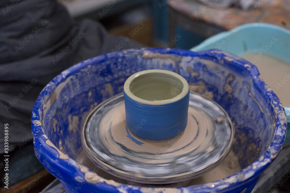 Clolored clay cup stands on a potter's wheel. Pottery hobby. Handcrafted earthenware Clolored clay cup stands on a potter's wheel. Pottery hobby. Handcrafted earthenware
