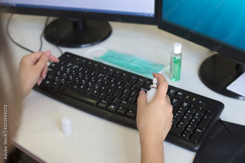 Female hands spray disinfectant spray on computer keyboard. Antibacterial processing of office equipment Female hands spray disinfectant spray on computer keyboard. Antibacterial processing of office equipment
