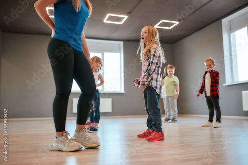 Cute little girl is talking with her female dance teacher while standing in the dance studio. Group of cute little boys and girls studying modern dance in choreography class