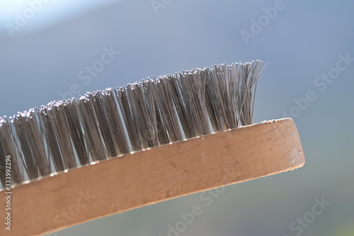 A diagonal wire brush in front of a blurred background.