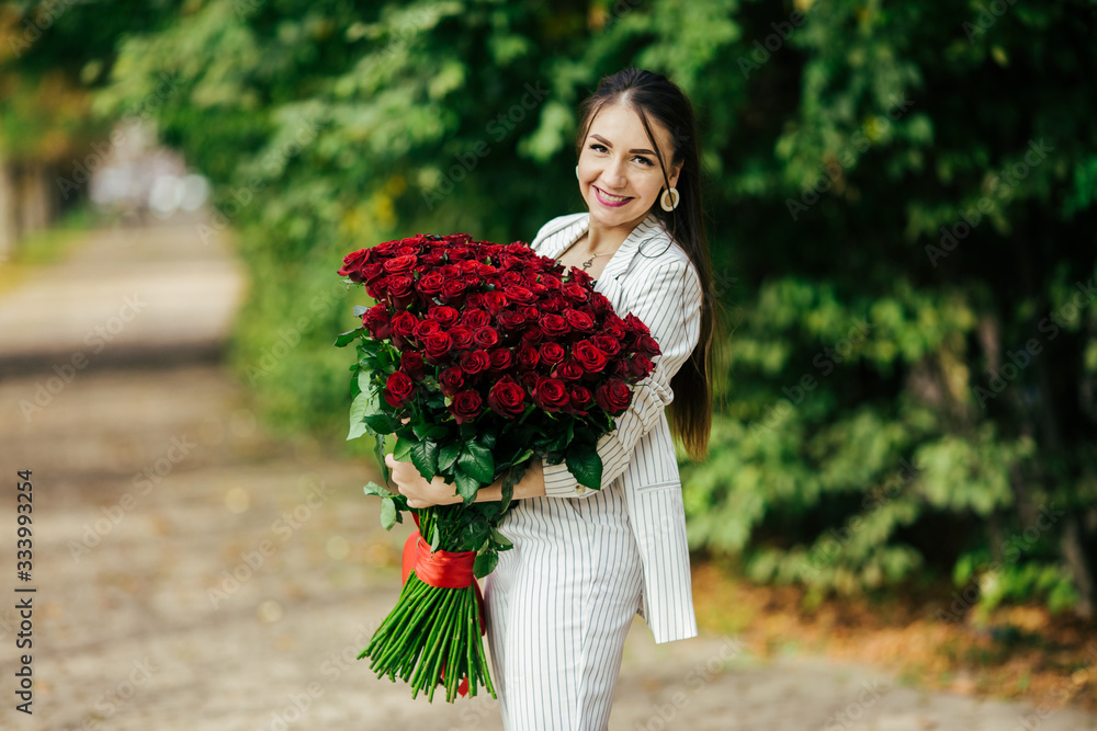 Fototapeta premium Valentine's Day 101 Birthday Gift For You. Beautiful woman with stylish makeup. Girl holding a gorgeous big bouquet of roses. Perfect sensual lips. Fashion Makeup. Woman in earrings