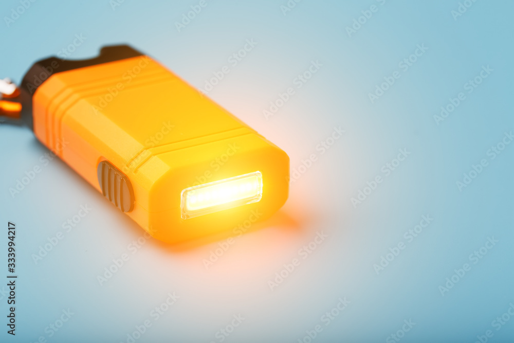 Orange led Flashlight with a carabiner on a blue background. LED lights in flight. Orange led Flashlight with a carabiner on a blue background. LED lights in flight.
