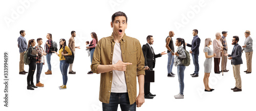 Shocked young man pointing to a large group of people talking