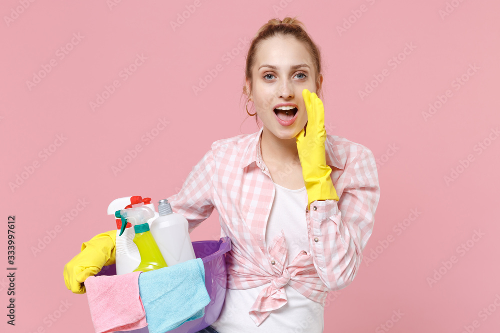 Woman housewife in rubber gloves hold basin with detergent bottles washing cleansers doing housework isolated on pink background. Housekeeping concept. Whispering secret behind her hand, sharing news. Woman housewife in rubber gloves hold basin with detergent bottles washing cleansers doing housework isolated on pink background. Housekeeping concept. Whispering secret behind her hand, sharing news.