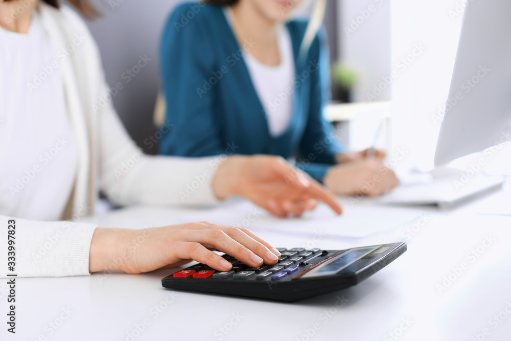 Accountant checking financial statement or counting by calculator income for tax form, hands closeup. Business woman sitting and working with colleague at the desk in office. Tax and Audit concept Accountant checking financial statement or counting by calculator income for tax form, hands closeup. Business woman sitting and working with colleague at the desk in office. Tax and Audit concept