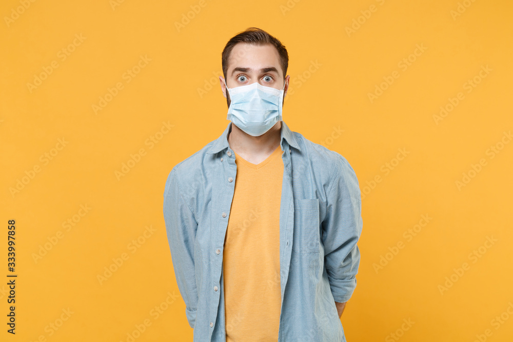 Shocked young man in casual clothes, sterile face mask posing isolated on yellow background studio portrait. Epidemic pandemic rapidly spreading coronavirus 2019-ncov sars covid-19 flu virus concept. Shocked young man in casual clothes, sterile face mask posing isolated on yellow background studio portrait. Epidemic pandemic rapidly spreading coronavirus 2019-ncov sars covid-19 flu virus concept.