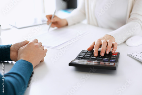 Accountant checking financial statement or counting by calculator income for tax form, hands closeup. Business woman sitting and working with colleague at the desk in office. Tax and Audit concept