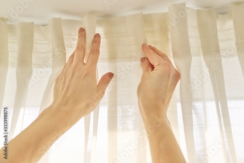 Close up of woman hands hanging curtain with metal hooks on ceiling ledge