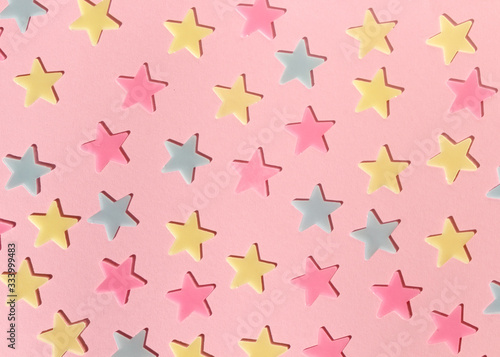 Close-up of yellow, blue and pink plastic stars on a pink background. Festive starry background. Flat lay