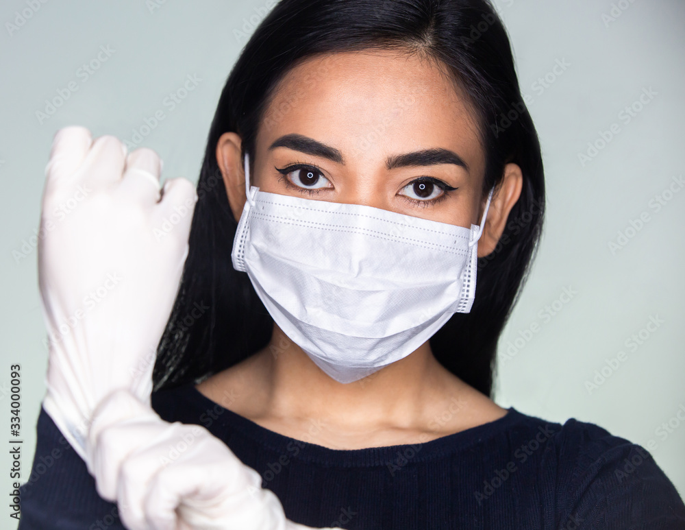 Coronavirus outbreak: An Asian woman putting on a medical rubber gloves and disposable mask to avoid contagious viruses. Preventing coronavirus transmission. Self protection. Coronavirus outbreak: An Asian woman putting on a medical rubber gloves and disposable mask to avoid contagious viruses. Preventing coronavirus transmission. Self protection.