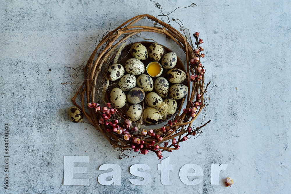 Easter wreath of grape branches, apricot flowers, quail feathers and eggs on light cement background. White letter EASTER. Copy space for greeting text, Happy Easter card, top view. Easter wreath of grape branches, apricot flowers, quail feathers and eggs on light cement background. White letter EASTER. Copy space for greeting text, Happy Easter card, top view.