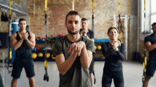 The fitness leader. Portrait of caucasian trainer showing exercises to diverse men and women during workout in industrial gym. Group training concept