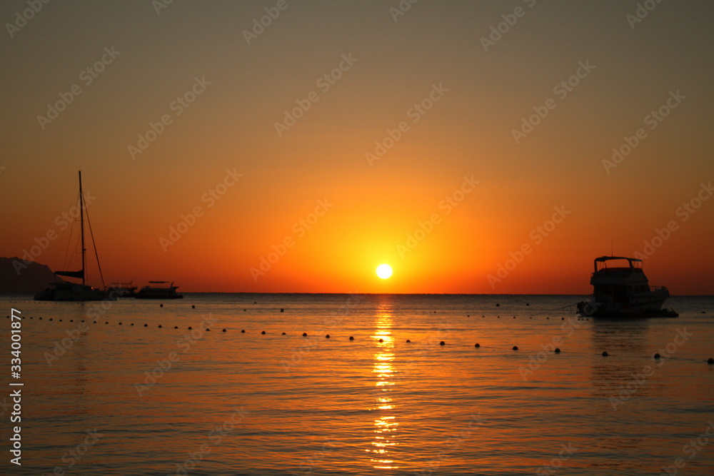 Black silhouettes of ships on a background of yellow sunset. A beautiful landscape photo with a ship against the setting sun. Sea or river port with ships, boats.