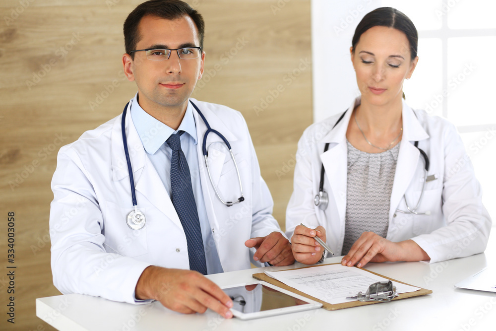 Middle aged doctor man filling up medical documents or prescription with his female colleague. Group of doctors at work discussing treatment problems while sitting at a desk in hospital. Data in Middle aged doctor man filling up medical documents or prescription with his female colleague. Group of doctors at work discussing treatment problems while sitting at a desk in hospital. Data in