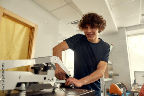 One. Two. Three. Done. Young cheerful male worker using heat press transfer machine for printing t-shirt at workplace