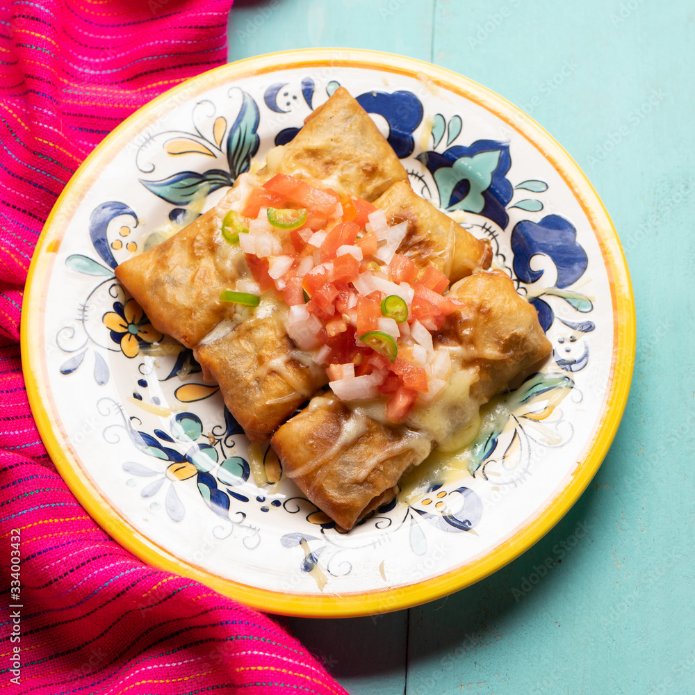 Mexican chimichanga with melted cheese and pico de gallo sauce on turquoise background