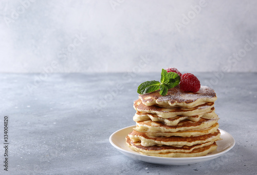 American cuisine. Breakfast. Pancakes with raspberries, powdered sugar and mint in a white plate on a light grey background. Background image, copy space