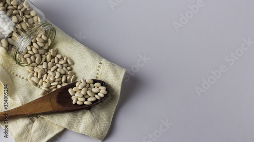  Beans in a glass jar on a cloth napkin and with a wooden spoon. White background. Top view