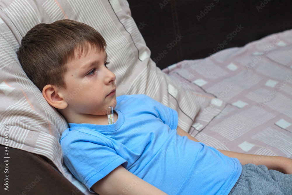 A child with a thermometer measures the temperature while lying on the bed. Sick child. Virus. flu.covid-19 A child with a thermometer measures the temperature while lying on the bed. Sick child. Virus. flu.covid-19