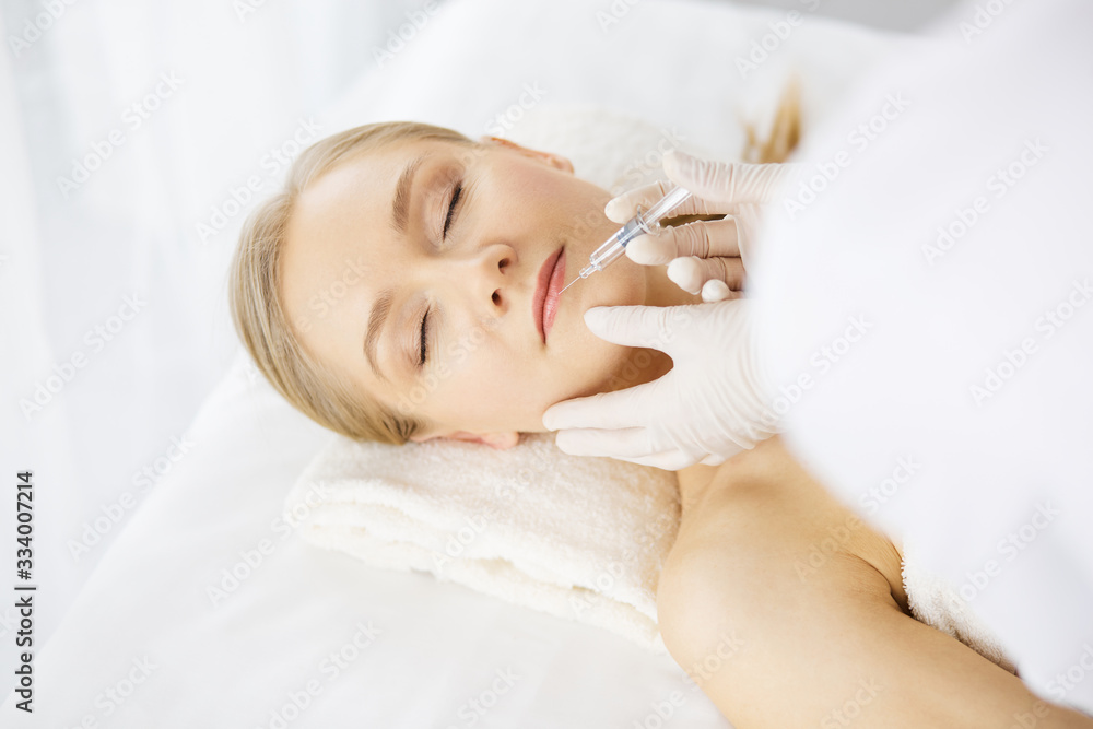 Beautician doctor doing beauty procedure with syringe to caucasian female face. Cosmetic medicine and surgery, beauty injections concept Beautician doctor doing beauty procedure with syringe to caucasian female face. Cosmetic medicine and surgery, beauty injections concept