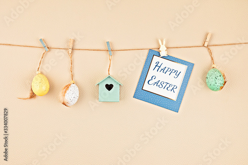 Easter greeting card hanging on the string with cute easter accessories over beige background