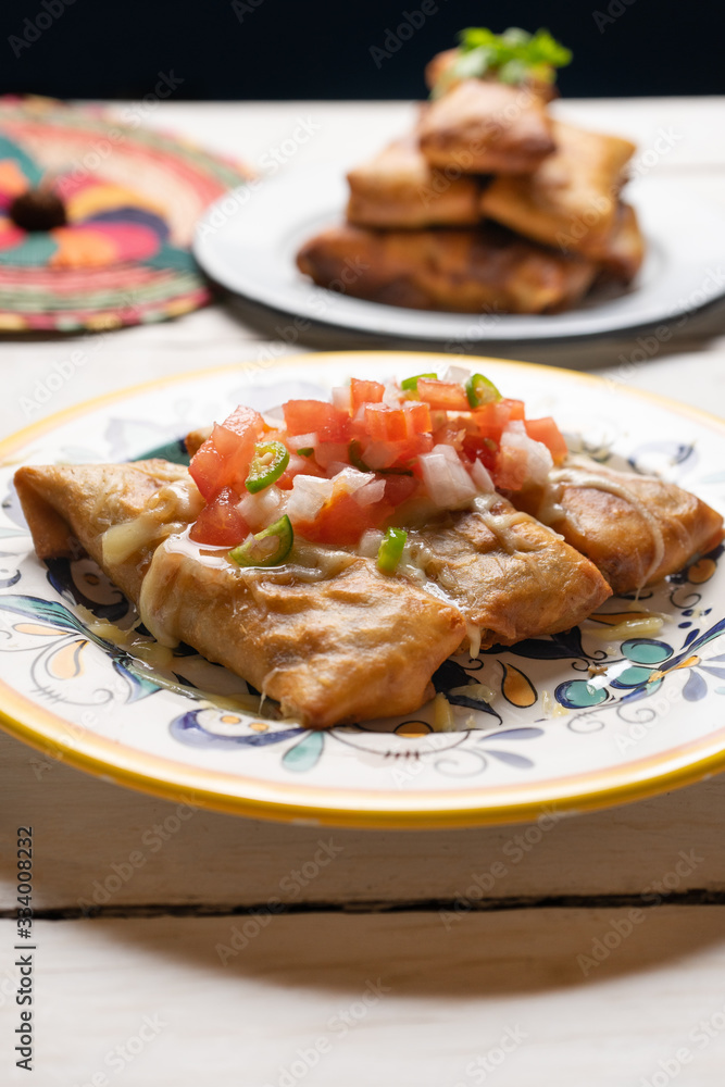 Mexican chimichanga with melted cheese and pico de gallo sauce on white background Mexican chimichanga with melted cheese and pico de gallo sauce on white background