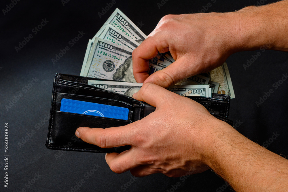 Man on black background holds in his hands a wallet with dollars close up.