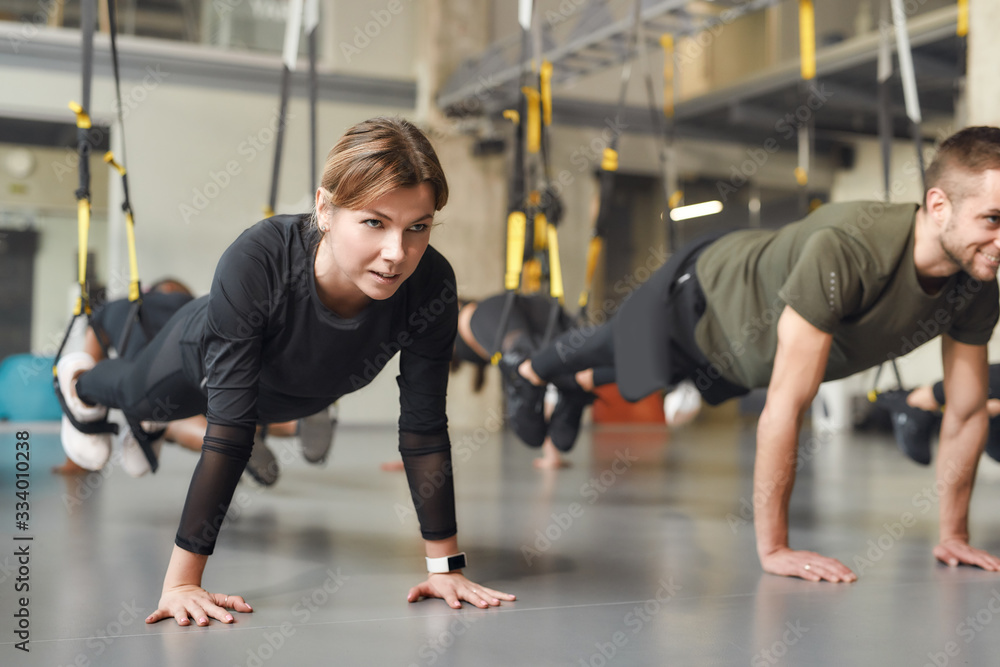 The only bad workout is no workout. Young woman stretching her body while doing fitness TRX training exercises at industrial gym. Straps, group workout concept The only bad workout is no workout. Young woman stretching her body while doing fitness TRX training exercises at industrial gym. Straps, group workout concept