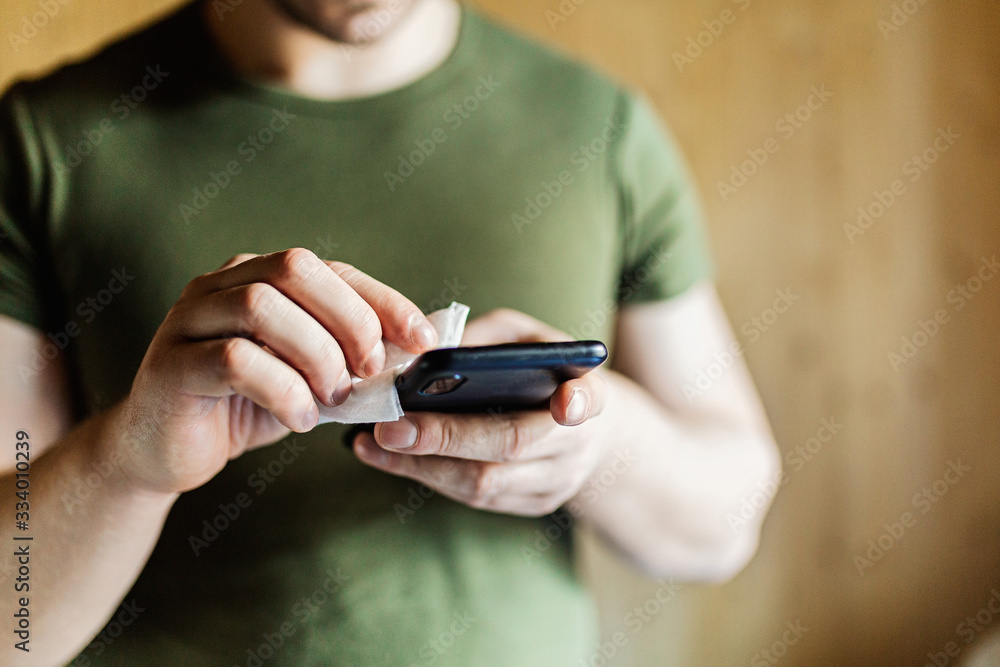 Disinfection the phone with an antiseptic using an antibacterial cloth. Close-up of hands holding a napkin with antiseptic, wiping the smartphone, covid-19 and coronavirus. Concept of personal hygiene Disinfection the phone with an antiseptic using an antibacterial cloth. Close-up of hands holding a napkin with antiseptic, wiping the smartphone, covid-19 and coronavirus. Concept of personal hygiene