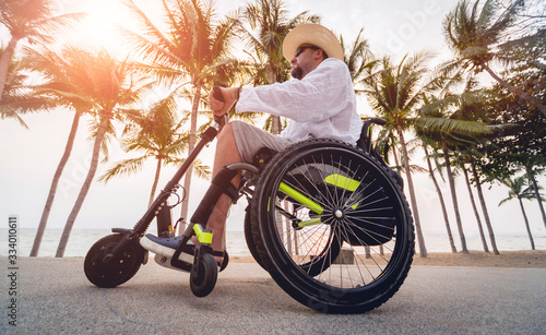 Disabled man in a wheelchair with electric scooter on the beach photo