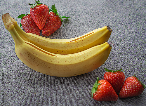 Fotografie Fresas jugosas y plátanos,  sobre un fondo gris