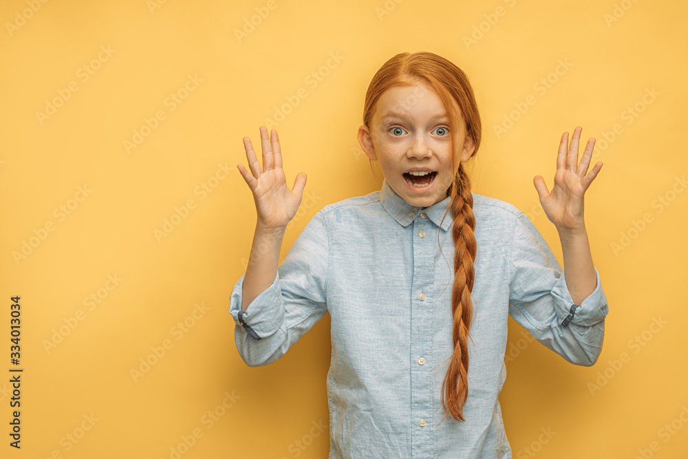 portrait of shocked caucasian girl with natural red hair, isolated over yellow background. happy child surprisingly react on news, stand with opened mouth and arms up, shout at camera portrait of shocked caucasian girl with natural red hair, isolated over yellow background. happy child surprisingly react on news, stand with opened mouth and arms up, shout at camera