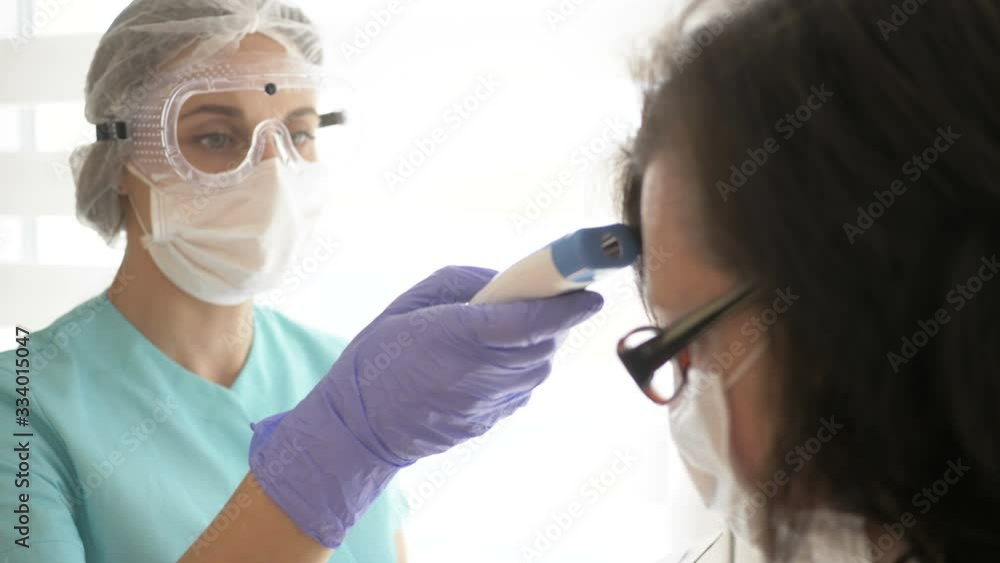 Nurse in a medical mask, glasses and gloves measures the patient's temperature with a non-contact infrared thermometer. Nurse in a medical mask, glasses and gloves measures the patient's temperature with a non-contact infrared thermometer.