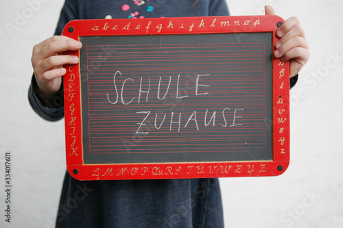Kind hält Tafel mit Schule Zuhause Schriftzug