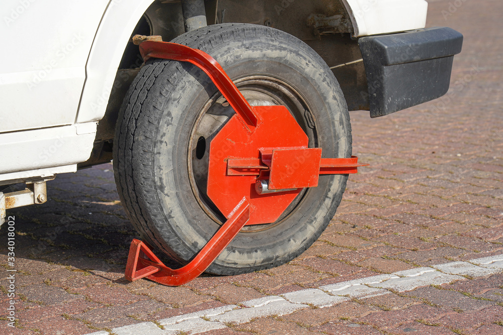 Fototapeta premium Parking Wheel Lock. Clamped front wheel of illegally parked car, red clamp attached to wheel. Car parked illegally is fined and wheel-locked by the police.