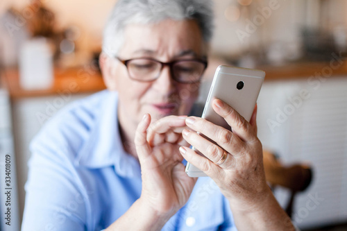 Senior woman using mobile phone at home. Retired person shopping online. People staying connected, virtual communication with gadget, delivery in social isolation. Pensioner reading news.