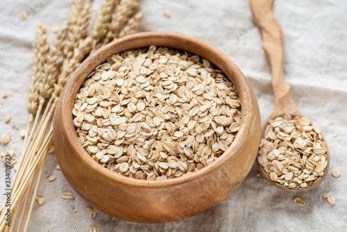 Rolled oats in wooden bowl on linen background. Healthy food, clean eating concept. Breakfast food uncooked oatmeal