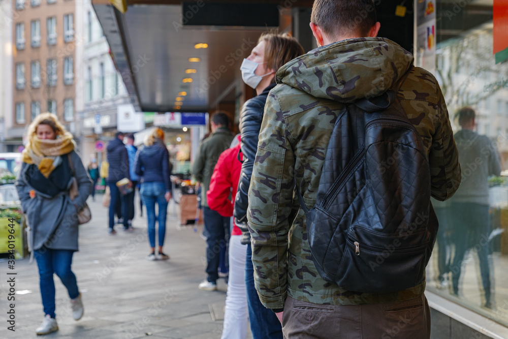 Selected focus, European people queue and wait on sidewalk outside in front of supermarket during quarantine for COVID-19 virus in Düsseldorf, Germany. Selected focus, European people queue and wait on sidewalk outside in front of supermarket during quarantine for COVID-19 virus in Düsseldorf, Germany.
