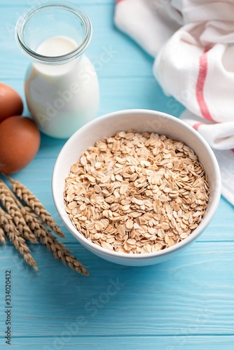 Oat flakes and bottle of milk on blue wooden table background. Ingredients for cooking oatmeal or healthy oat cookies