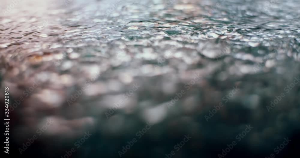Slow motion of autumn rain drops falling into puddle at night. Urban lights mirror reflection on water surface. Close up of raining outside in wet season. Rainy evening in modern city street Slow motion of autumn rain drops falling into puddle at night. Urban lights mirror reflection on water surface. Close up of raining outside in wet season. Rainy evening in modern city street